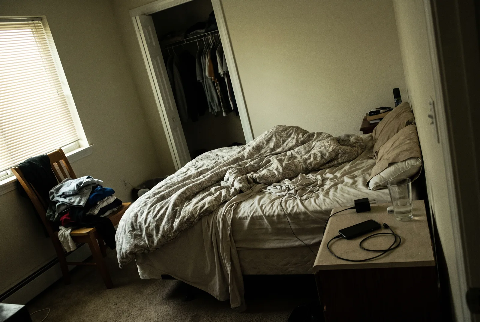 Bedroom as a dim phone snapshot with an unmade bed and clutter