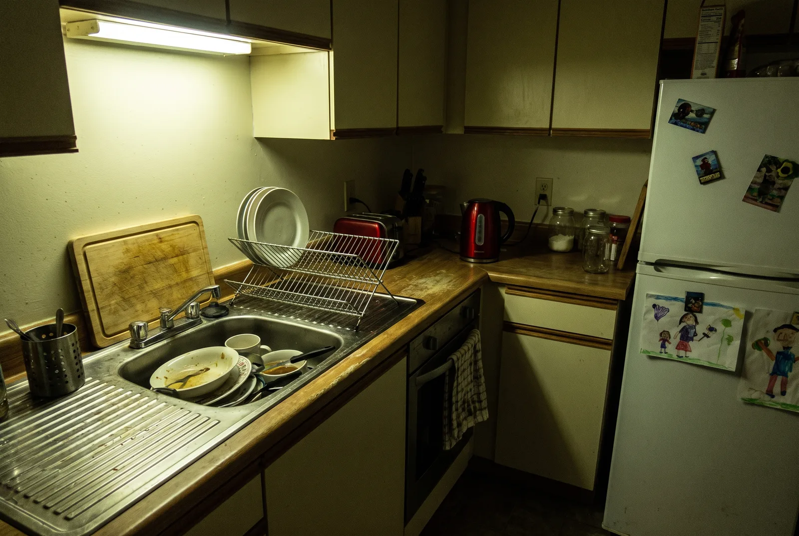 Kitchen as a dim phone snapshot with dishes in the sink under harsh yellow light